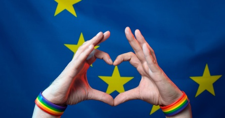 Men's hands with bracelets with LGBT symbols folded a heart from their fingers against the background of the European Union flag