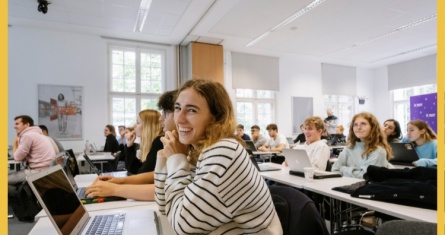 Student on a laptop in a lecture hall smiling